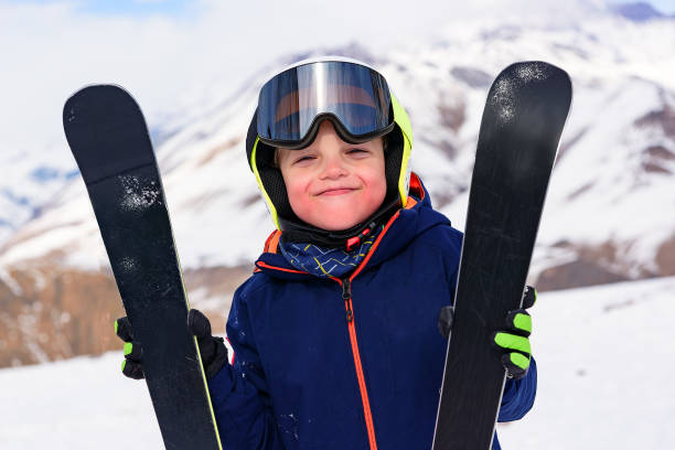 山でスキー休暇で幸せな小さな男の子。子供のスポーツとスキートレーニング。下り坂でスキーをした後に休む。 - sports helmet powder snow ski goggles skiing ストックフォトと画像