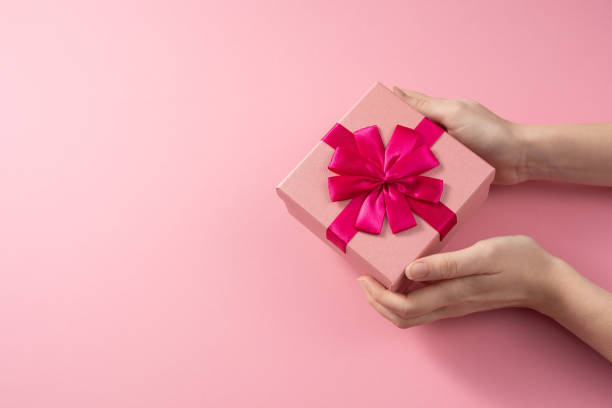 istock Valentine's Day celebration concept. A nice gift from a loved one. Box with a bow in female hands on a delicate pink background. Copy space. Flat lay. 1203506792