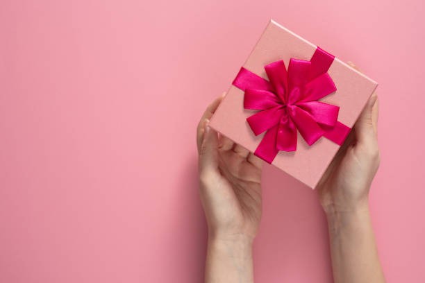 istock Valentine's Day celebration concept. A nice gift from a loved one. Box with a bow in female hands on a delicate pink background. Copy space. Flat lay. 1203506818