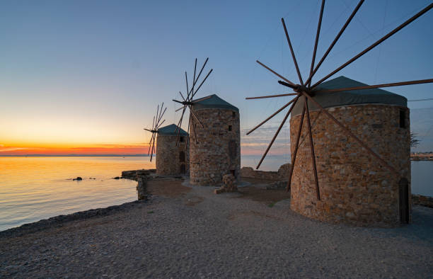 Old traditional windmills on beach of Chios Town on Chios Island in Greece at golden sunrise.
