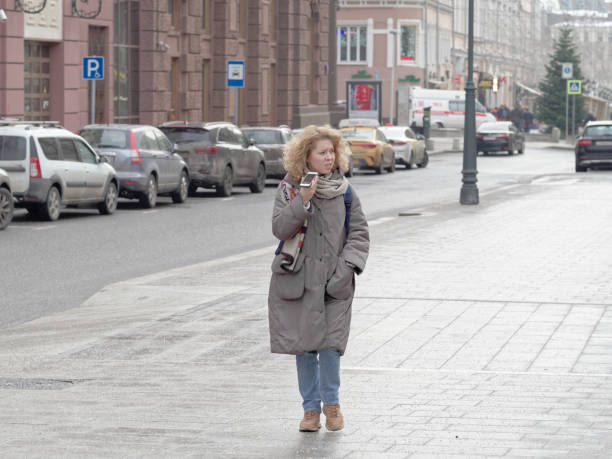 Moscow, Russia - February 01: a young woman is using smartphone while walking on the street