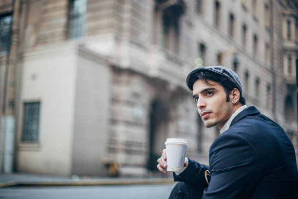 Handsome, elegant man with hat is drinking takeaway coffee on the street.