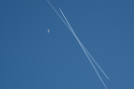 half moon in the open sky and two planes passing by and their traces.