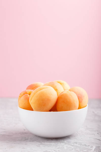 istock Fresh orange apricots in white bowl on gray and pink pastel background. side view, copy space, selective focus. 1203517632