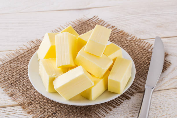 istock Rectangular pieces of fresh yellow butter on a white saucer and table knife over a white wooden table. Dairy. Sandwich butter. Natural fat nutrient. 1203519118