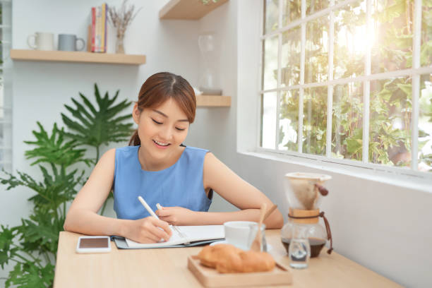 istock Smiling young Asian female entrepreneur sitting at a table and writing down notes 1203520162