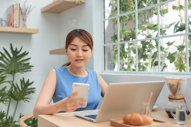 istock Happy young Asian woman using phone and laptop while working at home behind window. 1203521028