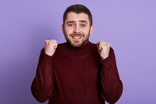 retrato interno de homem carismático emocional de boa aparência com punhos de barba apertando, fazendo gesto, sorrindo sinceramente, se divertindo, recebendo boas notícias, estando em alto astral. conceito de pessoas. - high minded - fotografias e filmes do acervo