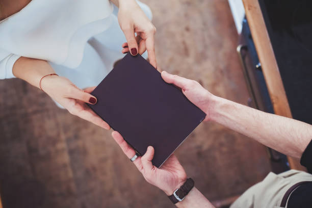 Male and female hands holding a book in a black cover. Male and female hands holding a book in a black cover. Relationship, gift.Copy space. book display stock pictures, royalty-free photos & images