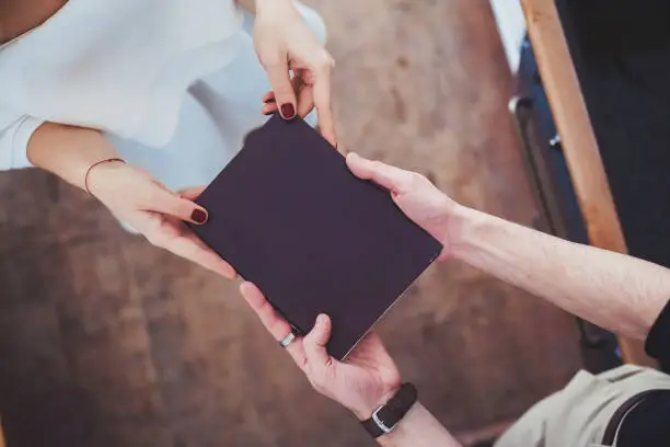 Photo of Male and female hands holding a book in a black cover.