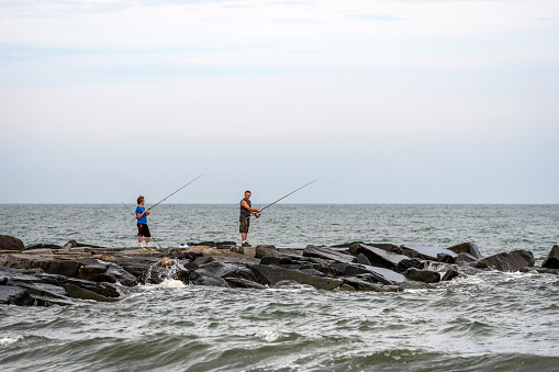 Atlantic city, New Jersey - june 18, 2019:  Two fishermen on a stone pier on the ocean coast