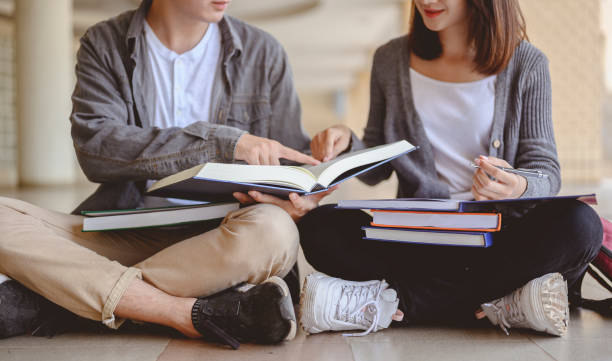 istock Education, Learning, Student, Campus, University, Lifestyle concept. Two students are sitting on the floor reading books to education. Study for test preparation in University. 1203530494