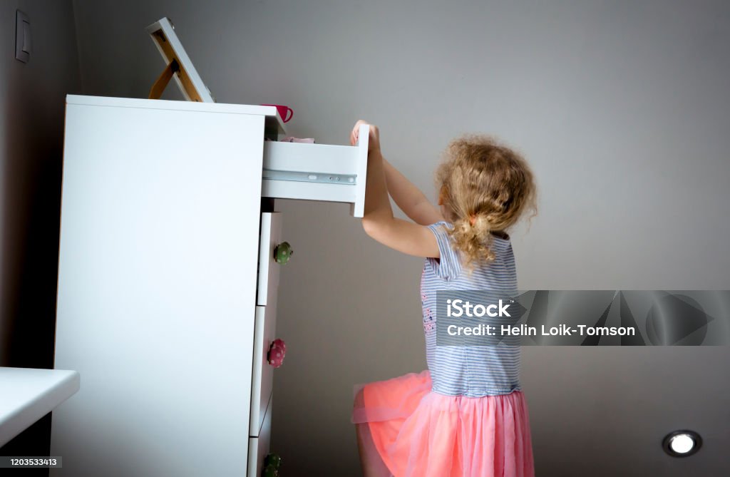 Junges Mädchen Kind Klettern auf modernen High-Dresser-Möbel, Gefahr der Kommode Tauchen über Konzept. Kinder zu Hause Gefahren. Inszeniertes Foto. - Lizenzfrei Möbel Stock-Foto