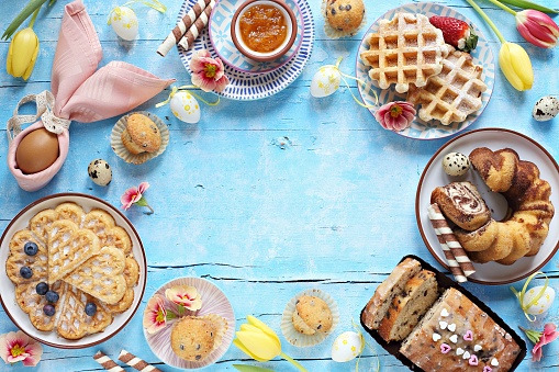 Easter festive dessert table with various of cakes, waffles and sweets. Blue background. Overhead view