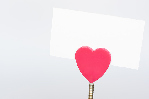 A red heart shape paper holder and a white paper on white background