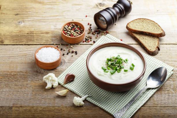 white vegetable cream soup of cauliflower in a brown clay plate on a wooden background. - cauliflower vegetable portion cabbage imagens e fotografias de stock