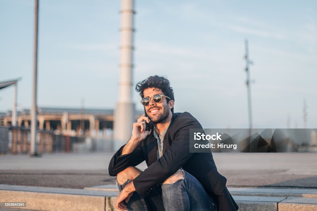 Stylish man talking on smart phone Handsome man in black, elegant jacket sitting outdoors and talking on smart phone. Business Casual Stock Photo