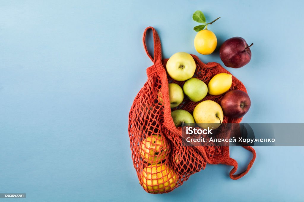 Apples and lemons in an orange string bag on a blue background. Top view. Apples and lemons in an orange string bag on a blue background. Top view. Concept of life without plastic. Horizontal orientation. Apple - Fruit Stock Photo