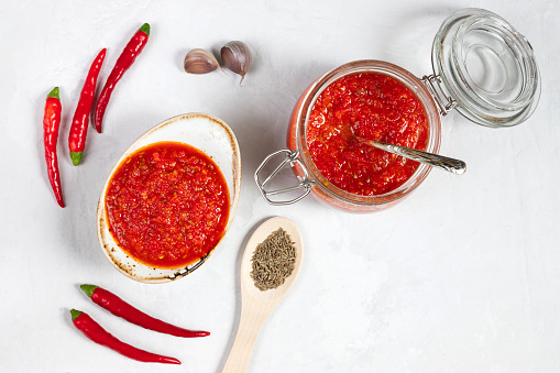 Hot chili pepper sauce paste harissa. Adjika on a white background. Traditional Tunisia, Georgian and Arabic cuisine. Homemade rose harissa in a bowl. Copy space. Flat lay, top view.
