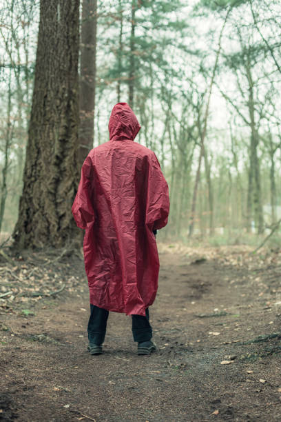 istock Man in red raincoat on forest trail. Rear view. 1203545632