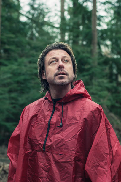 istock Middle aged man in red raincoat in woods. Looking up. 1203546233
