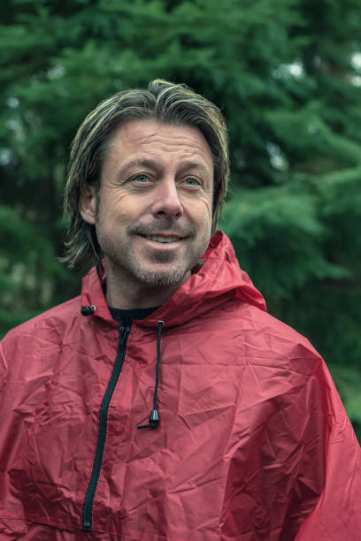 istock Smiling middle aged man in red raincoat in fir forest. 1203546493