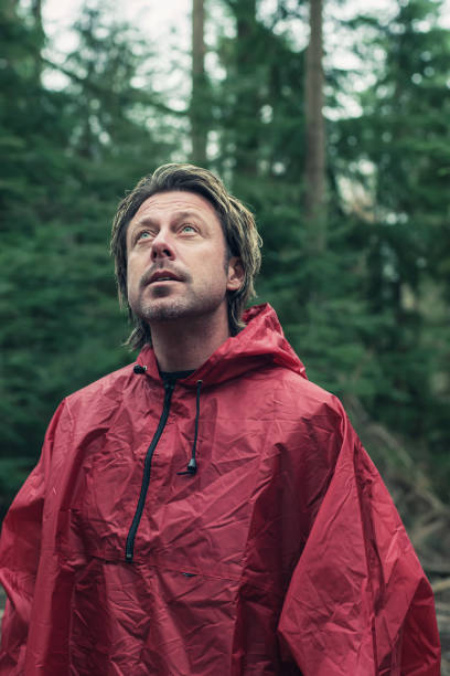 istock Middle aged man in red raincoat in woods. Looking up. 1203546630