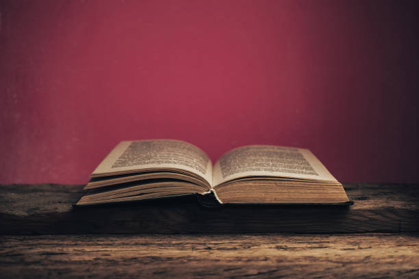 istock Old book on a old oak wooden table and red wall background behind. 1203546833