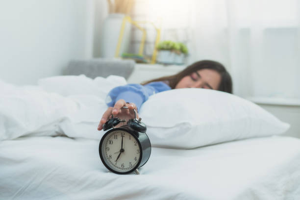 istock Woman's hand touch alarm clock on bed, lazy and rest time on holiday concept 1203555545