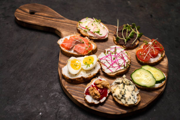istock Cooking healthy vegetarian sandwiches. Assorted whole grain vegetable bruschettas with microgreen. Eating right concept, food background. Fitness toasts menu. Sandwiches with creamy cheese, tofu, tomatos,  cucumber, eggs, salmon, blue cheese and microgree 1203563317