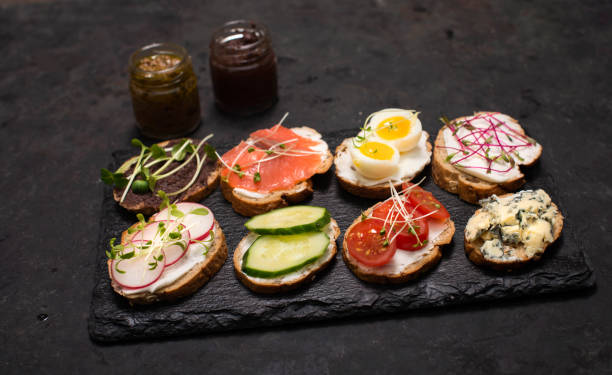 istock Healthy vegetarian sandwiches. Assorted whole grain vegetable bruschettas with microgreen. Eating right concept, food background. Sandwiches with creamy cheese, cucumber, eggs, salmon, blue cheese and microgreen on slate board. 1203563352