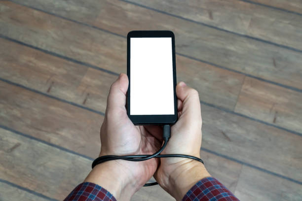 istock Social media obsession concept. Phone charging cable tangled around the hand 1203567538