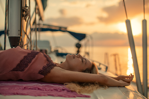 Attractive young woman on sailing enjoying and relaxing on deck. She wears pink pajamas and has a long blond hair.