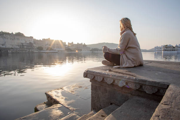 Mature woman explores a ghat at sunrise, looks out across lake Lake Pichola, Udaipur lake palace stock pictures, royalty-free photos & images