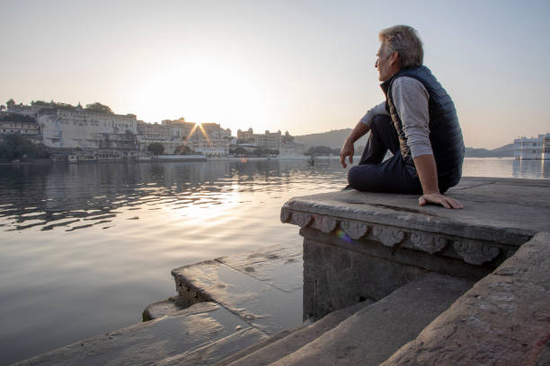 Mature man explores a ghat at sunrise, looks out across lake Lake Pichola, Udaipur lake palace stock pictures, royalty-free photos & images