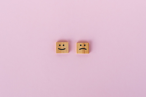 Sad and smiling symbol on wooden block, pink background.