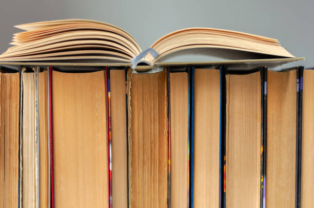 istock Open hardback book, diary, fanned pages on stack of books on white table in library. Books stacking. Back to school concept. Copy Space. Education learning background 1203580608