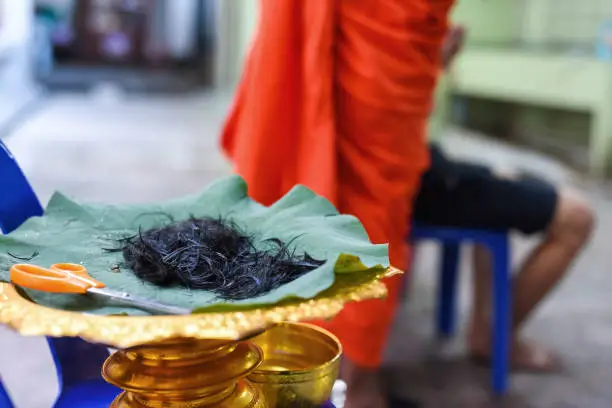 Cut hair on lotus leaf with blurred monk and ordained Thai man. Ordination ceremony of Thailand tradition. Religious and tradination believe.