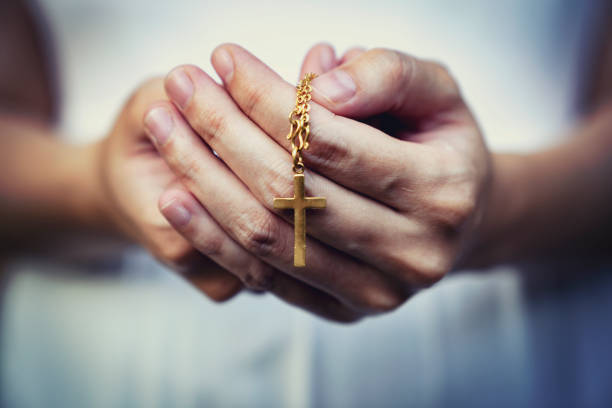 mains de femme priant retenant un chapelet de perles avec jésus christ dans la croix ou crucifix sur le fond noir. - prayer beads photos et images de collection