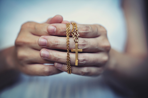 woman hands praying holding a beads rosary with Jesus Christ in the cross or Crucifix on black background.