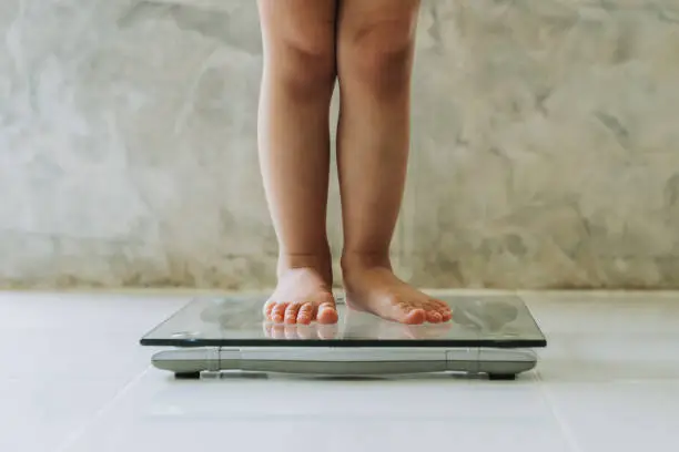 Photo of little girl on weight scale on floor background, Diet concept.
