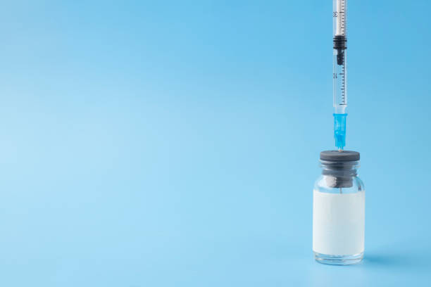 istock Medical glass bottle with copy space, with syringe inserted, on a blue background. Selective focus. Medical vial for injection with a syringe. 1203586403