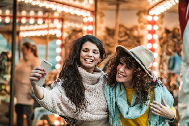 istock Two female friends taking selfie in amusement park 1203589343