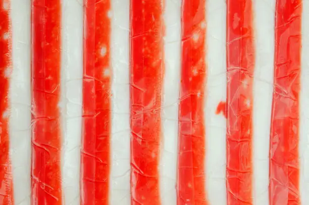 Photo of Background from crab sticks, top view. Texture of crab sticks in plastic packaging on a white background. White-red texture of crab sticks. Close-up, top view.