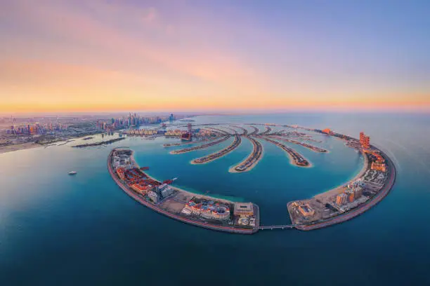 Photo of Aerial view of The Palm Jumeirah Island, Dubai Downtown skyline, United Arab Emirates or UAE. Financial district and business area in smart urban city. Skyscraper and high-rise buildings at sunset.