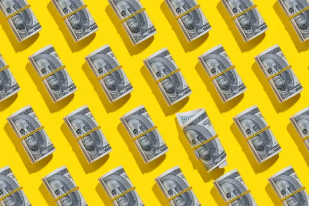 Repetitive one hundred dollar banknote rolls flat lay on yellow background