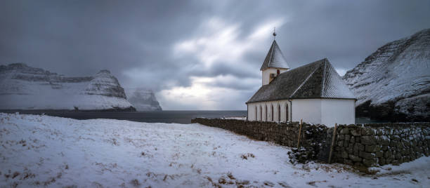 White church in snowy Vidareidi village with Bordoy and Kunoy islands in background, Faroe Islands