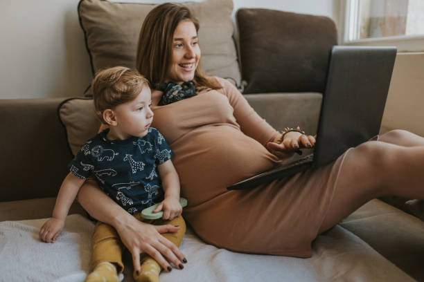 Pregnant woman using laptop and take care of her little son stock photo