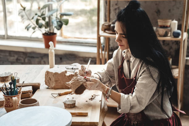 istock Craftsperson Concept. Young woman making pottery indoors making shape for clay using tool modeling smiling concentrated 1203615372