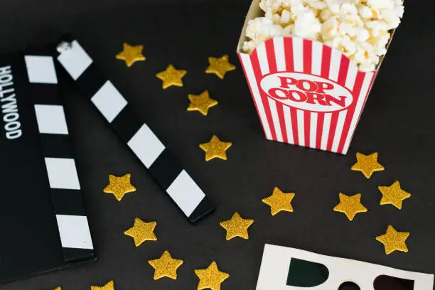 Flat lay photography with a clapboard, golden stars, 3D glasses and classic popcorn box on black background